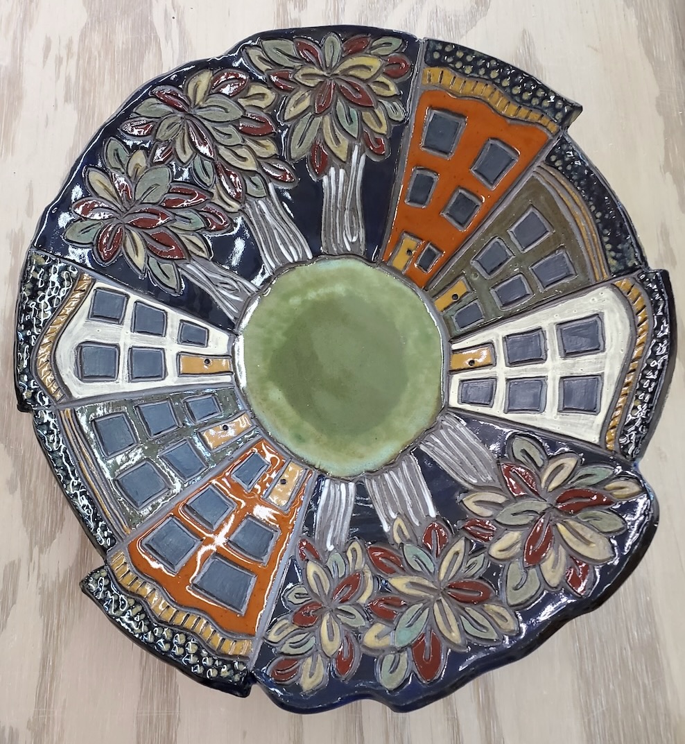 Carved ceramic plate with radial design of houses and trees